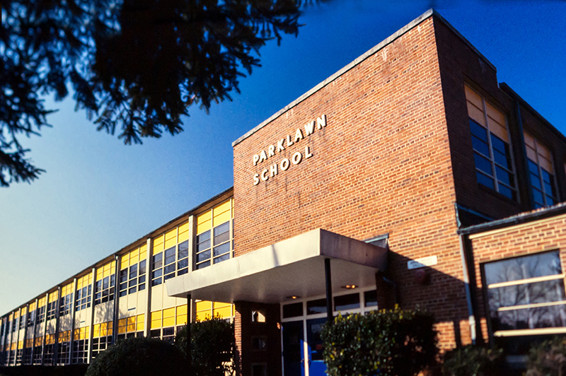 Color photograph from a 35 millimeter slide of the main entrance of Parklawn Elementary School taken in the late 1970s or early 1980s. The front of the building is painted yellow and the front doors are painted blue. 